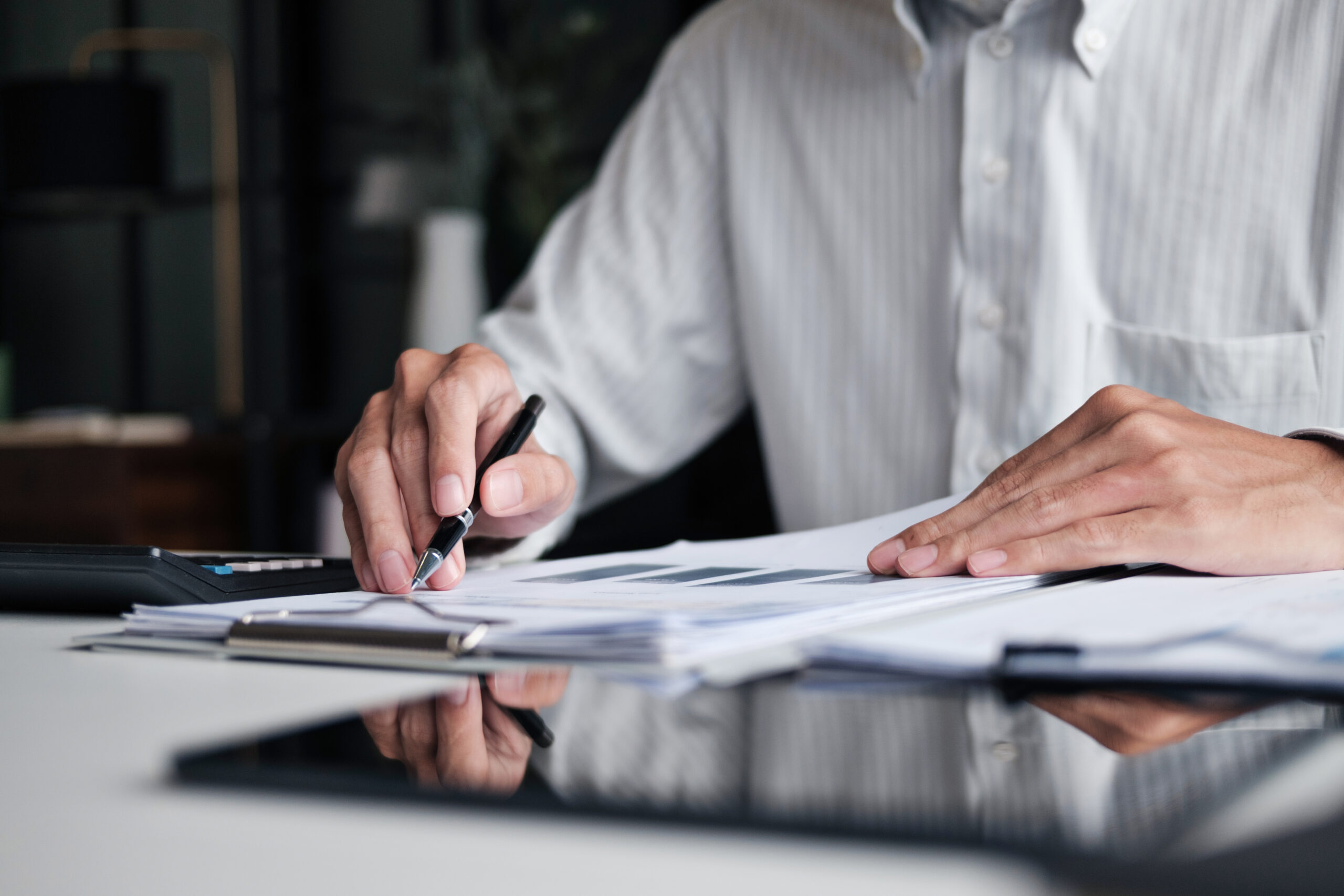 Focused businessman checking reports and verifying office documents with calculator and paper files